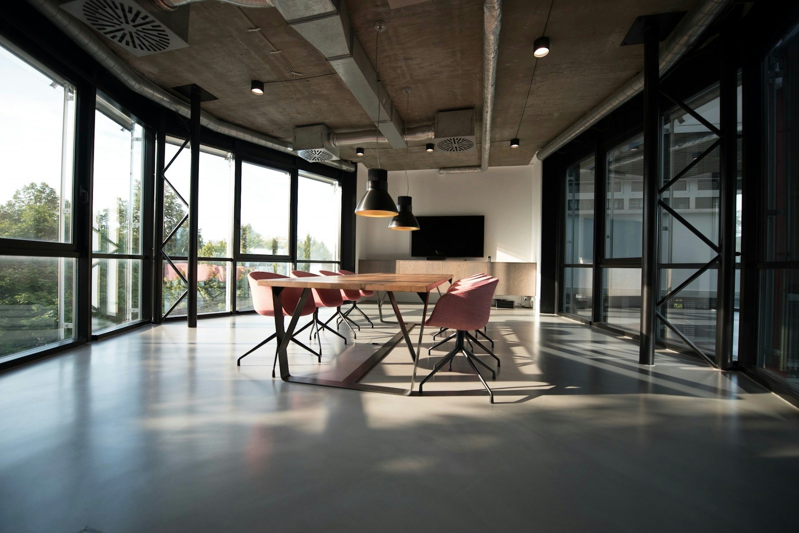 A sunlit modern workspace with glass walls and a long table